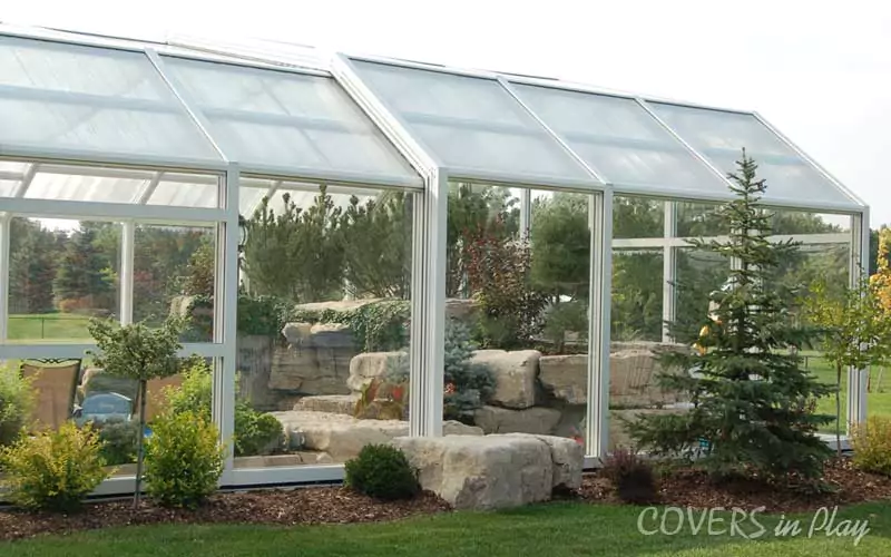 This image shows a side view of the exterior of a closed pool enclosure in Sharon, with lush greenery and backyard landscaping surrounding the structure.